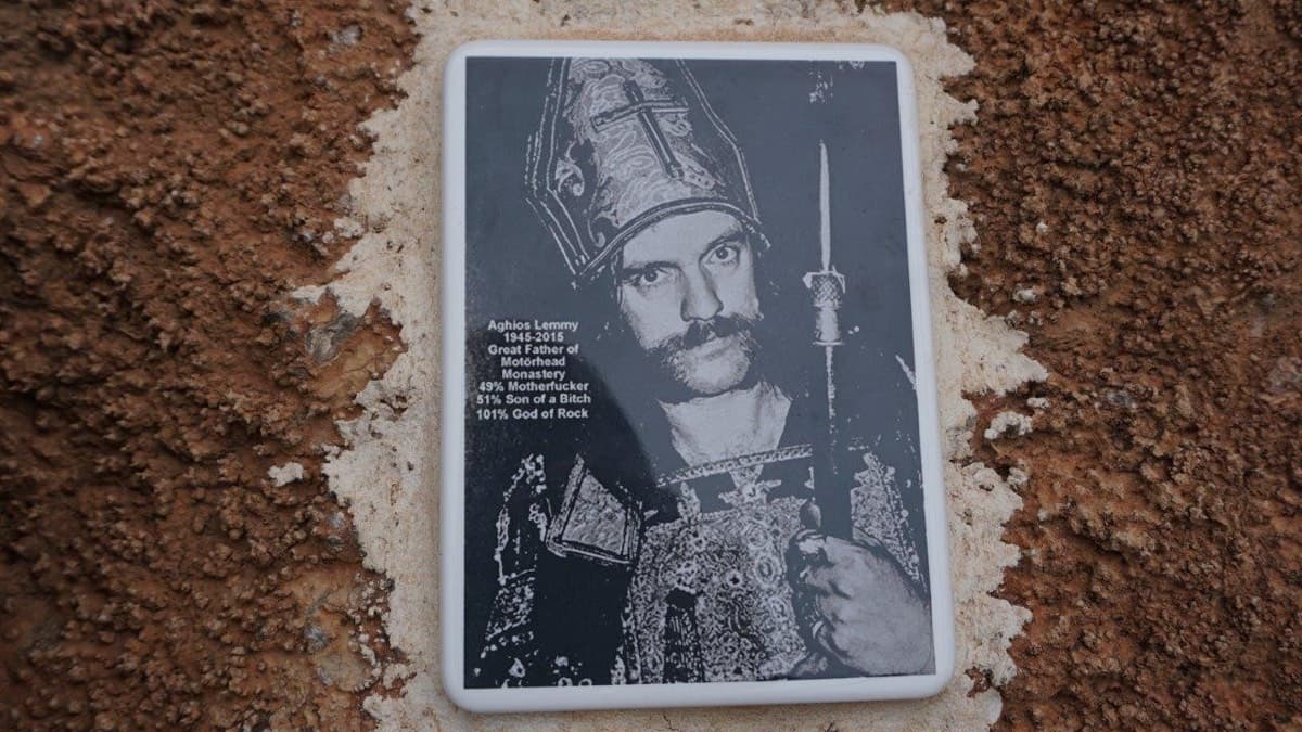 The 'Aghios Lemmy' plaque cemented to the red rock, from the camptocamp route page, which says the route name is marked at the foot of the route.