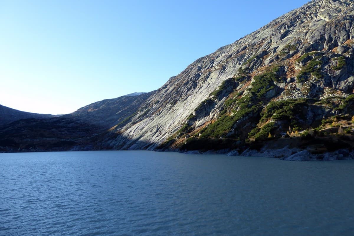 Crossing the Räterichsbodensee dam: the Seeplatten slabs rise from the far shore of the lake, in the sun.
