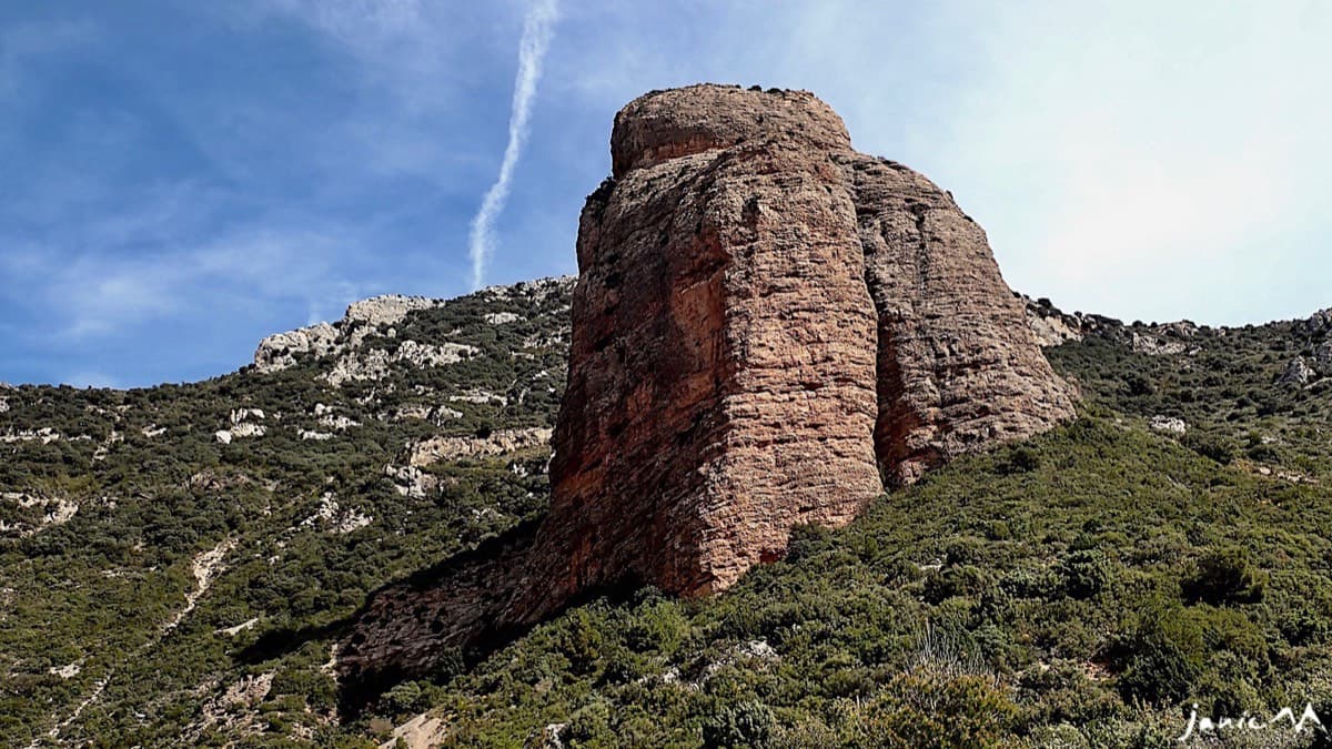 The Mallo Colorado standing alone above the scrub, seen from the barranco path; faint trails climb the slope to the foot of the face.