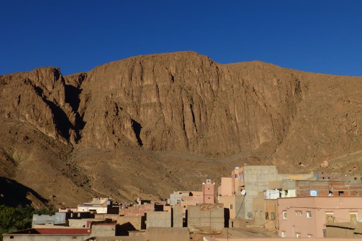 The Paroi du Levant above the houses of Tizgui, with the white inscription visible on the slope below the wall.