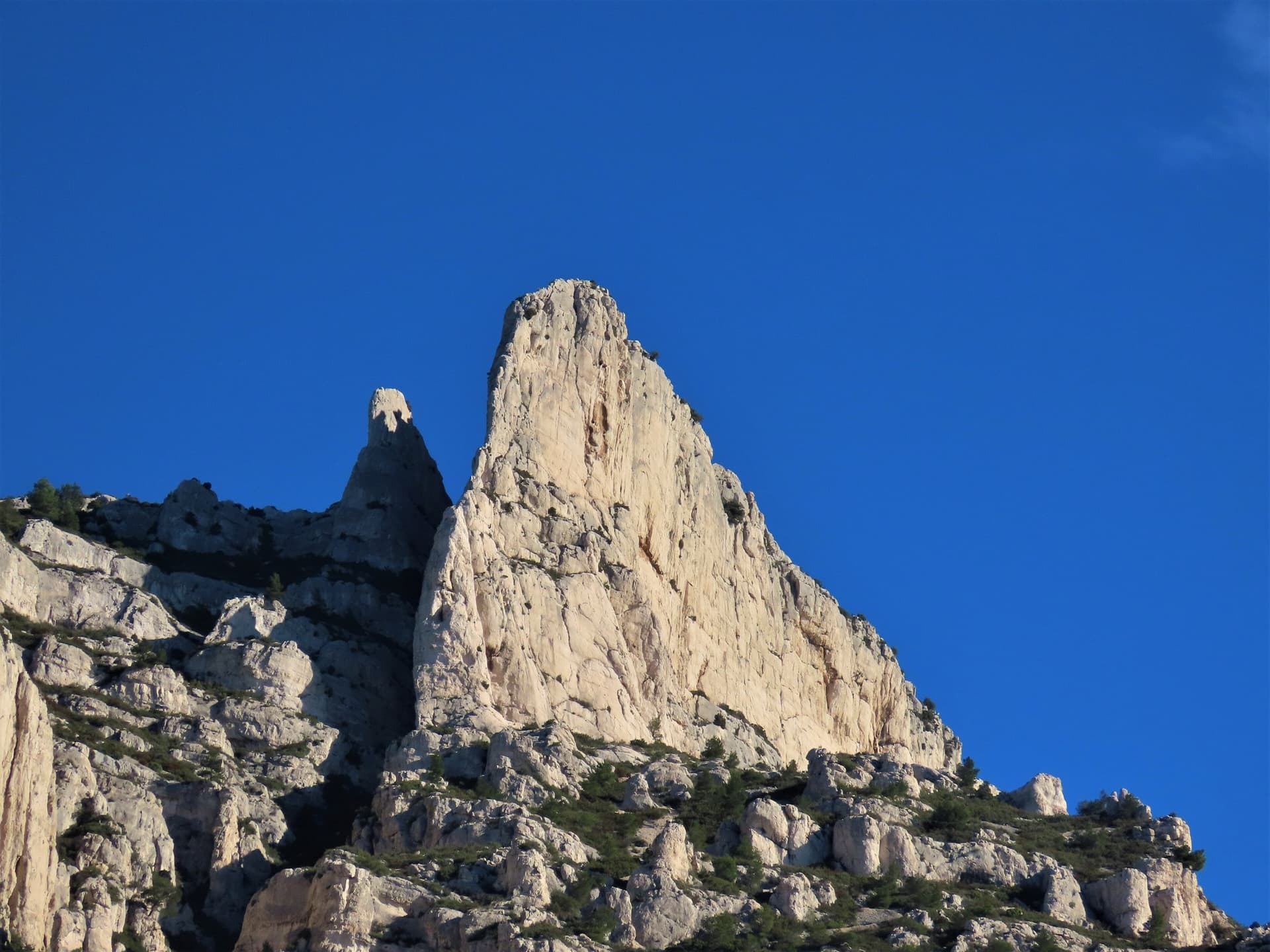 The spire of the Grande Candelle above its plinth of lower cliffs, seen from the Calanque de Sugiton; Armata Calanca climbs the plinth and then the south face to the summit, the line is not marked.