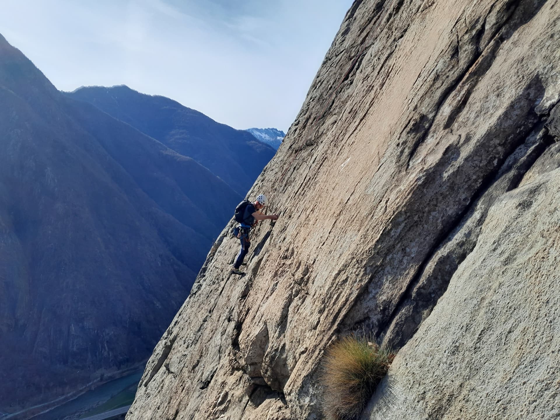 A climber on the sweeping gneiss slab of Bucce d'Arancia on the Paretone di Arnad (Corma di Machaby), with the Dora Baltea valley in shadow far below.