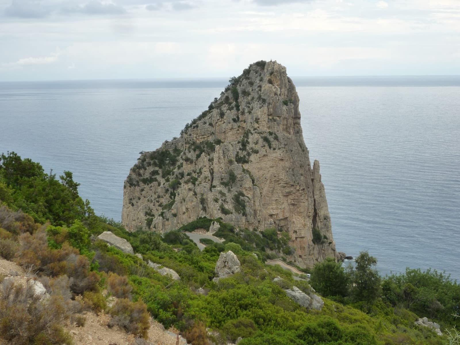 Pedra Longa from the road that descends to it, with the open sea behind.