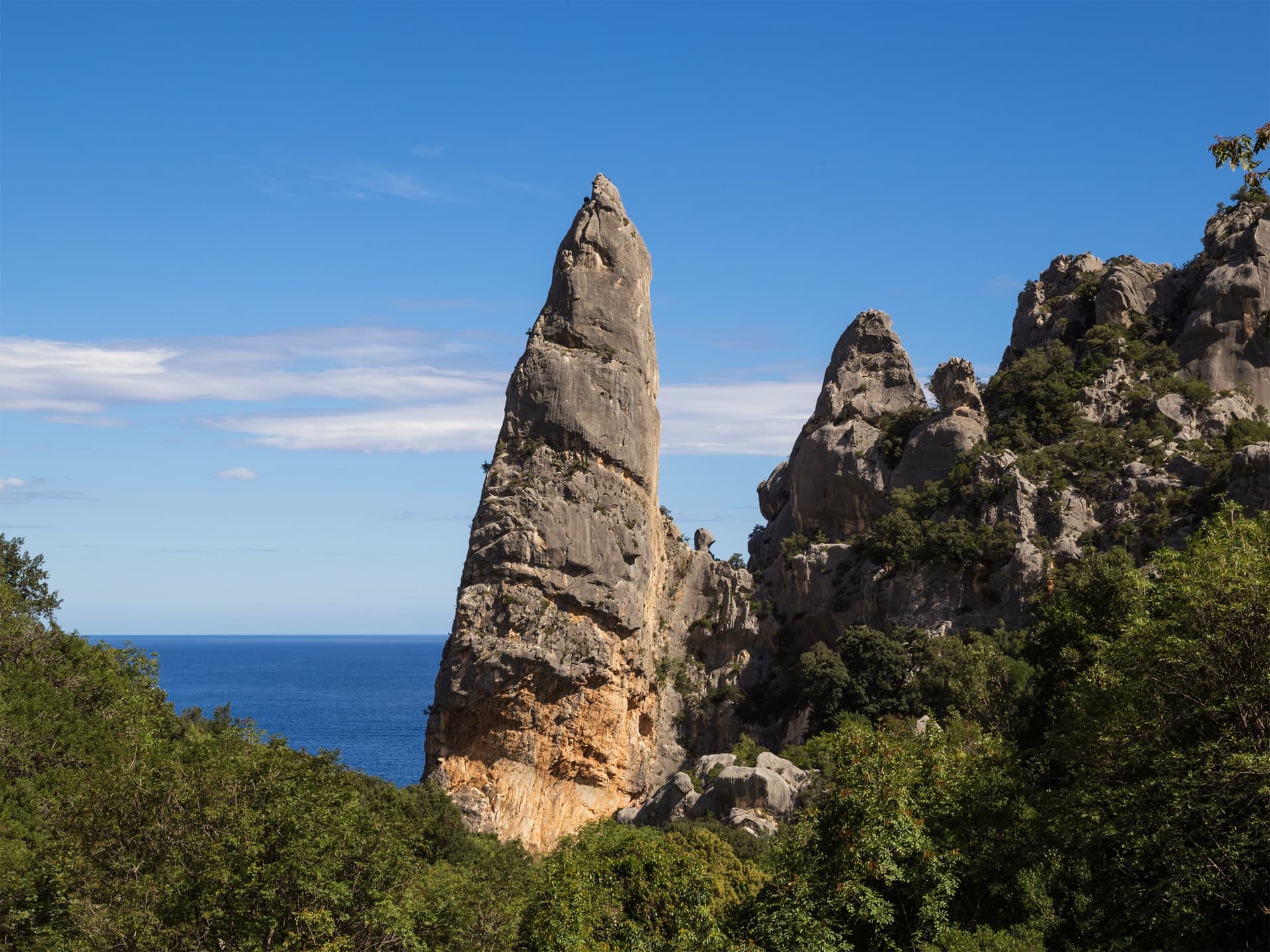 The Aguglia di Goloritzè, the 140 m limestone spire above Cala Goloritzè, seen from the approach path with the Gulf of Orosei behind.