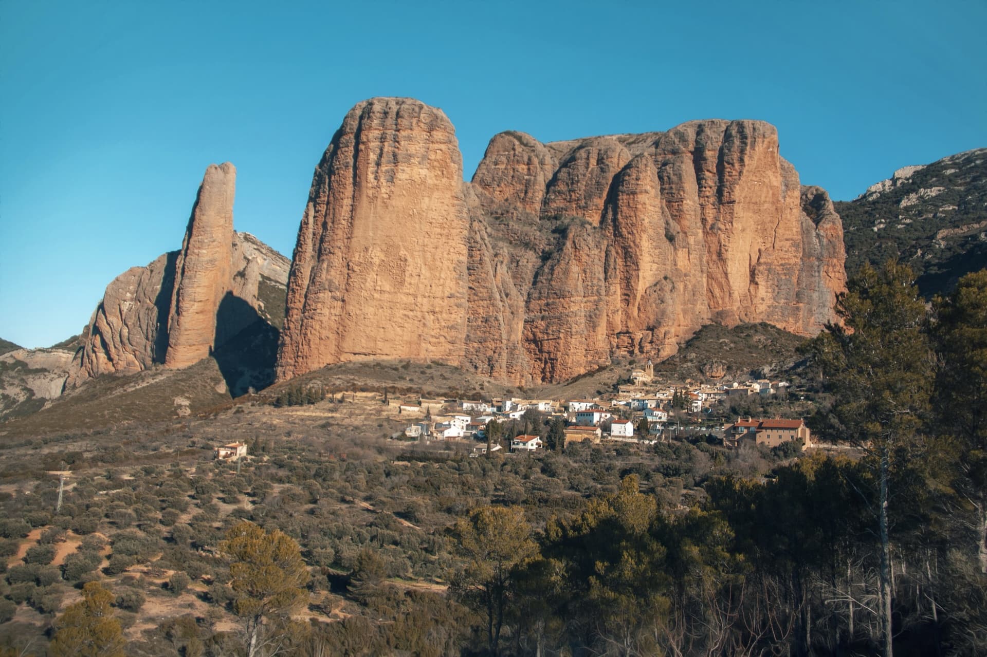 The classic view of Riglos from the south-west: the slender pinnacle of El Puro on the left, the great dome of Mallo Pisón beside it, and the main wall running right to La Visera above the village.