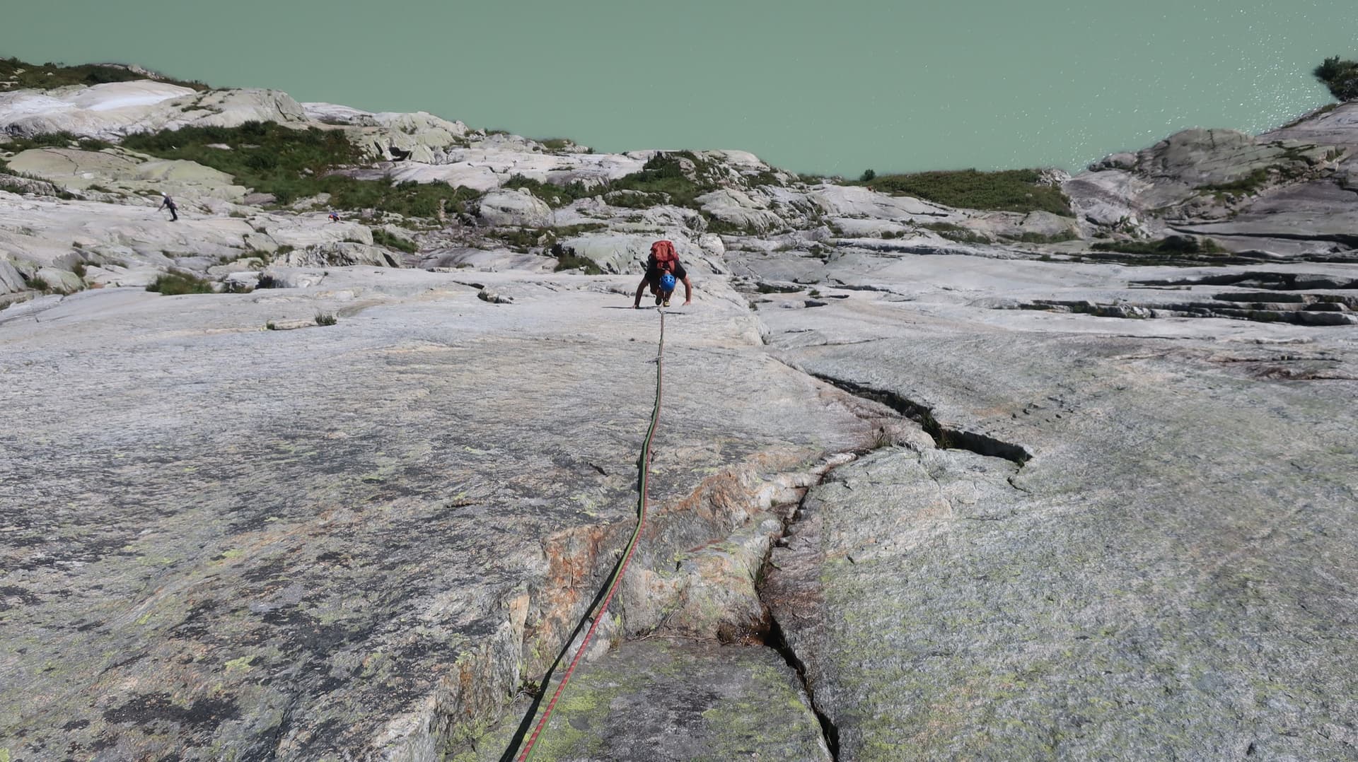 A climber on the pale granite of Grimselstrom, the Seeplatten slabs dropping to the milky green Räterichsbodensee.