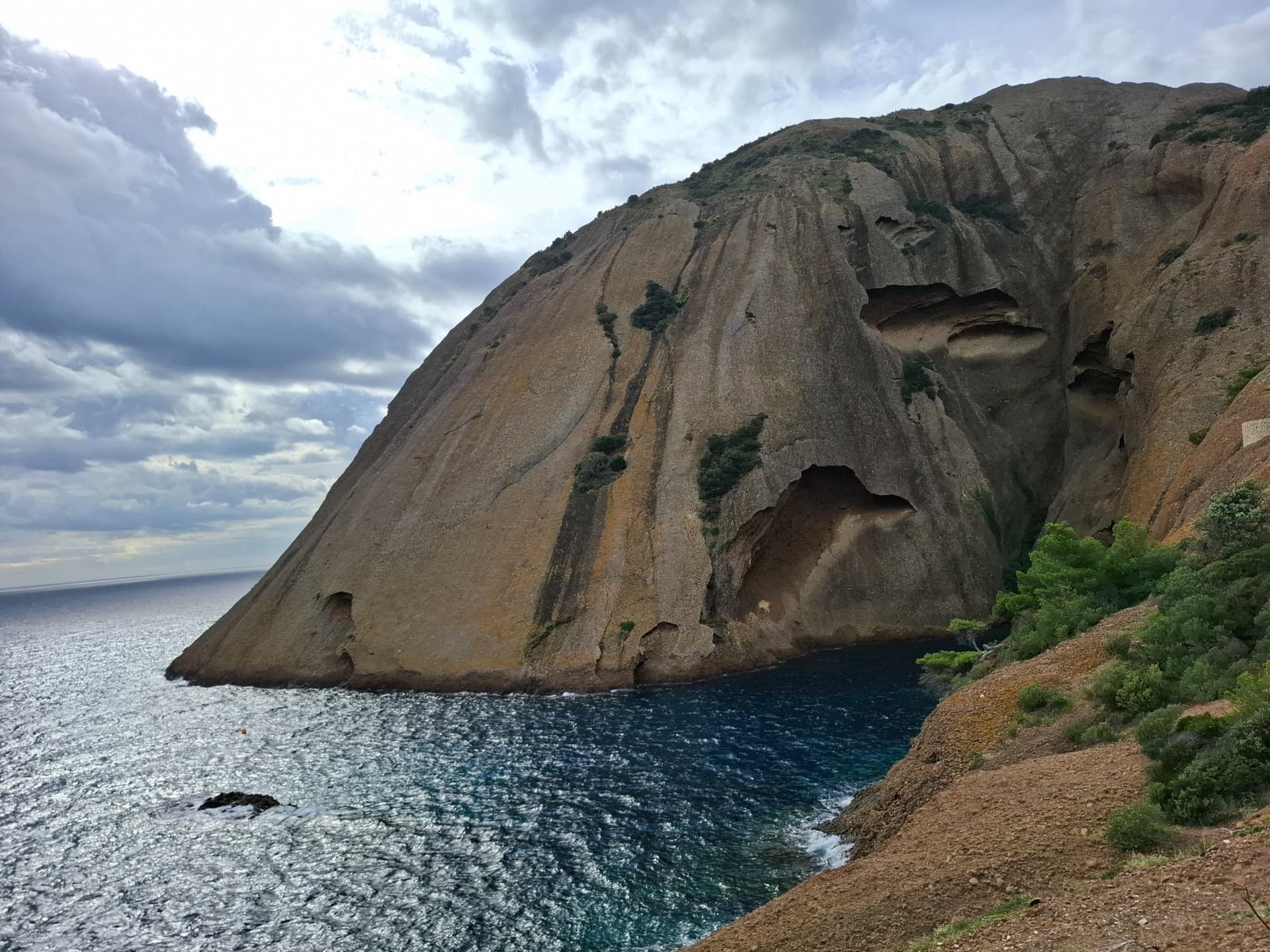 The east face of the Bec de l'Aigle, a single sweep of puddingstone falling into the Anse du Sec at La Ciotat, photographed on the approach to L'Atelier Bleu; the route climbs this face, the line is not marked.