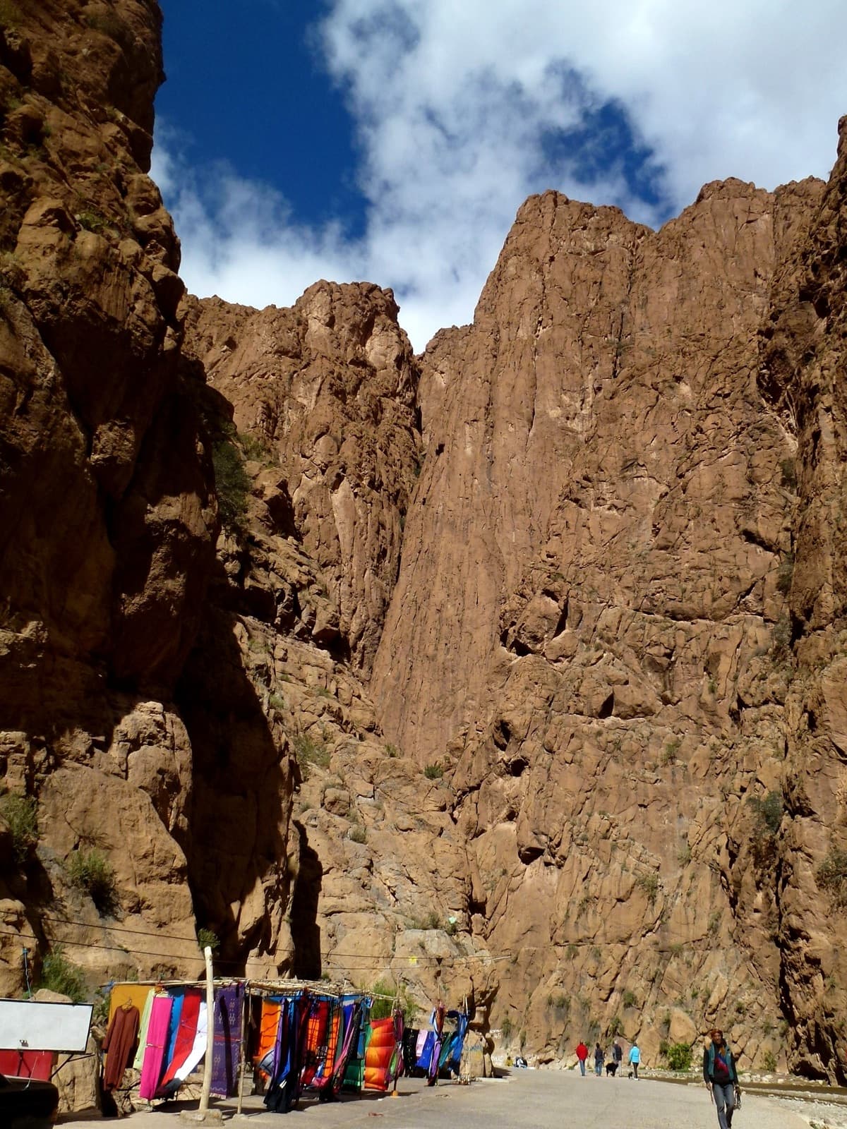 A tall grooved pillar above the souvenir stalls on the gorge road, with a deep gully on its left; it matches photographs of the Pilier du Couchant.