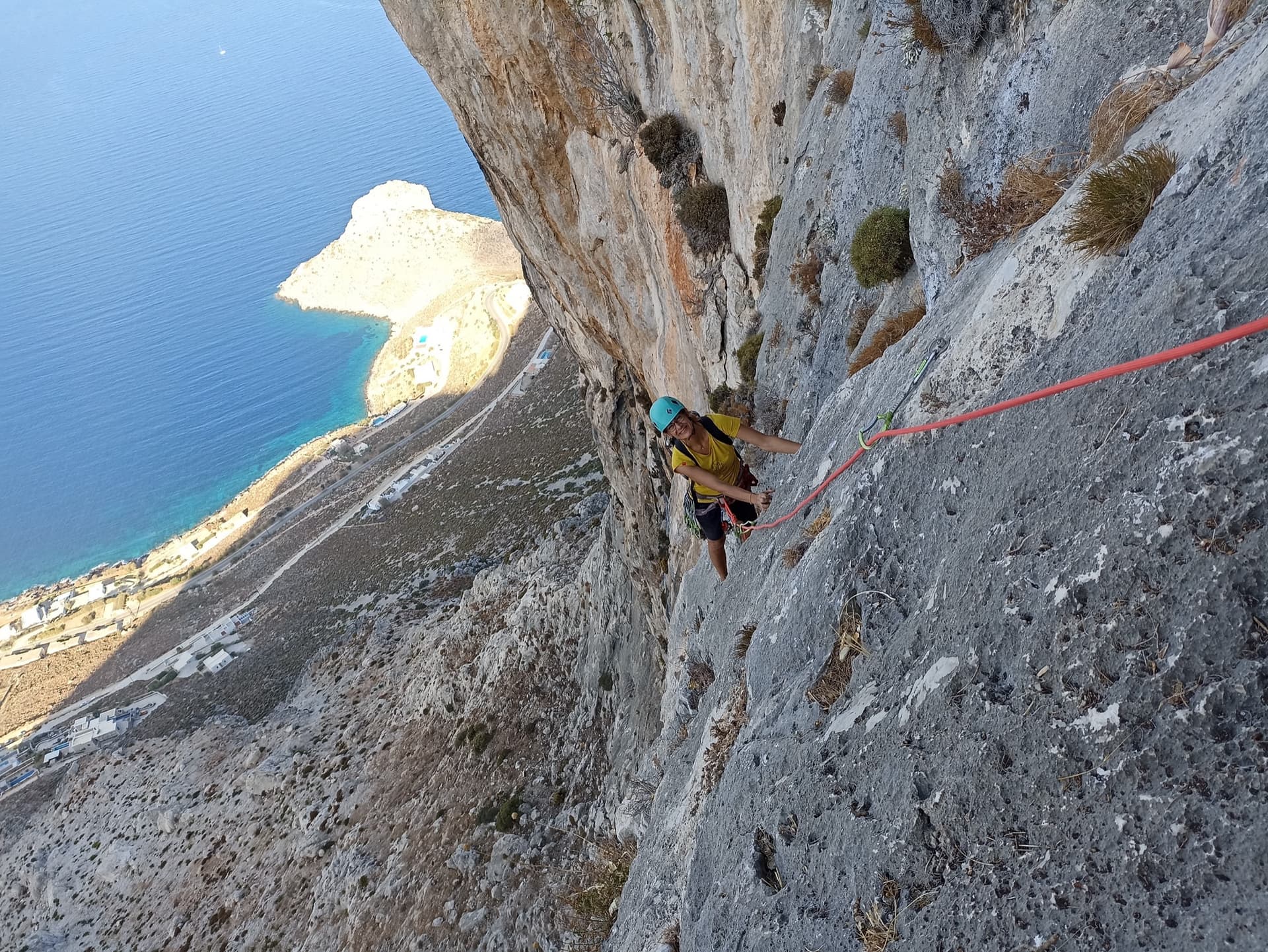 High on Lost Goat on the Olympic Wall: a climber on water-worn grey limestone with the Kalymnos coast far below.