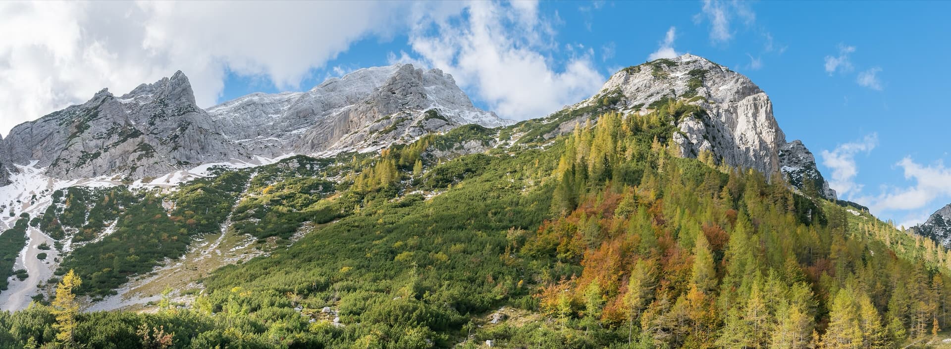 Mala Mojstrovka (left) and Nad Šitom glava (right) from the Vršič Pass in autumn; the routes are on the pale rock wall of Nad Šitom glava above the larches.