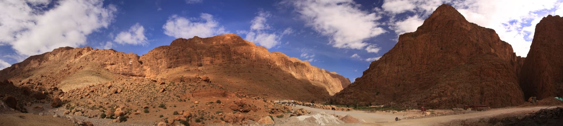 Panorama of the cliffs on the upstream side of the Todra narrows. The photographer lists the sectors from left to right as Can Güllich, Traînée Blanche, Scorpion, Jardins and the Aiguille d'Azrou; the Mur du Scorpion is in the band of cliffs above the scree slope.