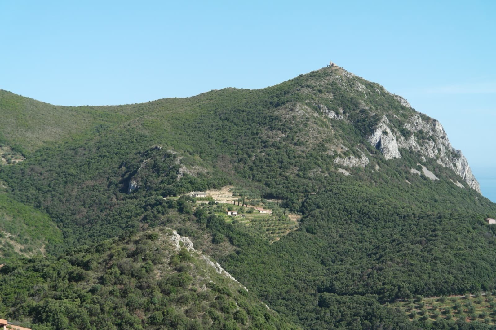 A tower-topped summit on the west coast of Monte Argentario with limestone crags falling towards the sea, photographed about 1.5 km north of Capo d'Uomo; it is very probably Capo d'Uomo and its watchtower seen from the north, not the south-east face the route climbs.