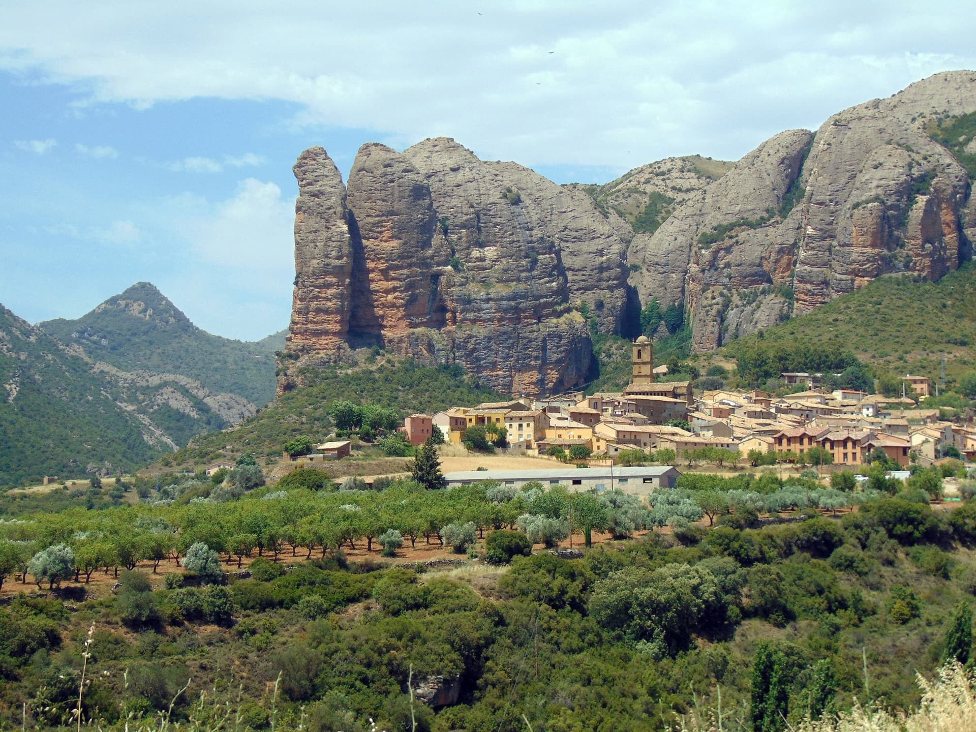 The Mallos de Agüero rising directly behind the village, seen from the south-east, with the detached tower of Peña Sola at the left end; the east-facing walls are towards the right-hand end of the massif.