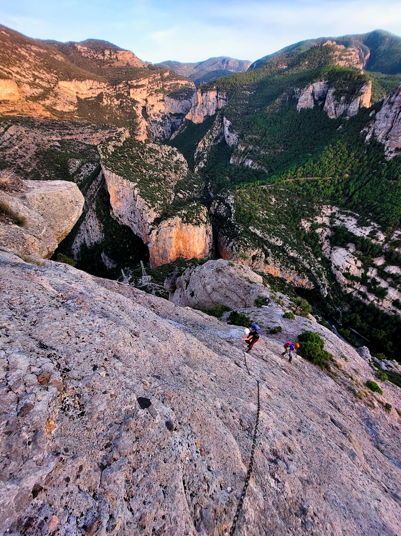 Looking down the grey conglomerate slabs of Performance on the Moles del Pessó, with two climbers below and the Collegats gorge behind