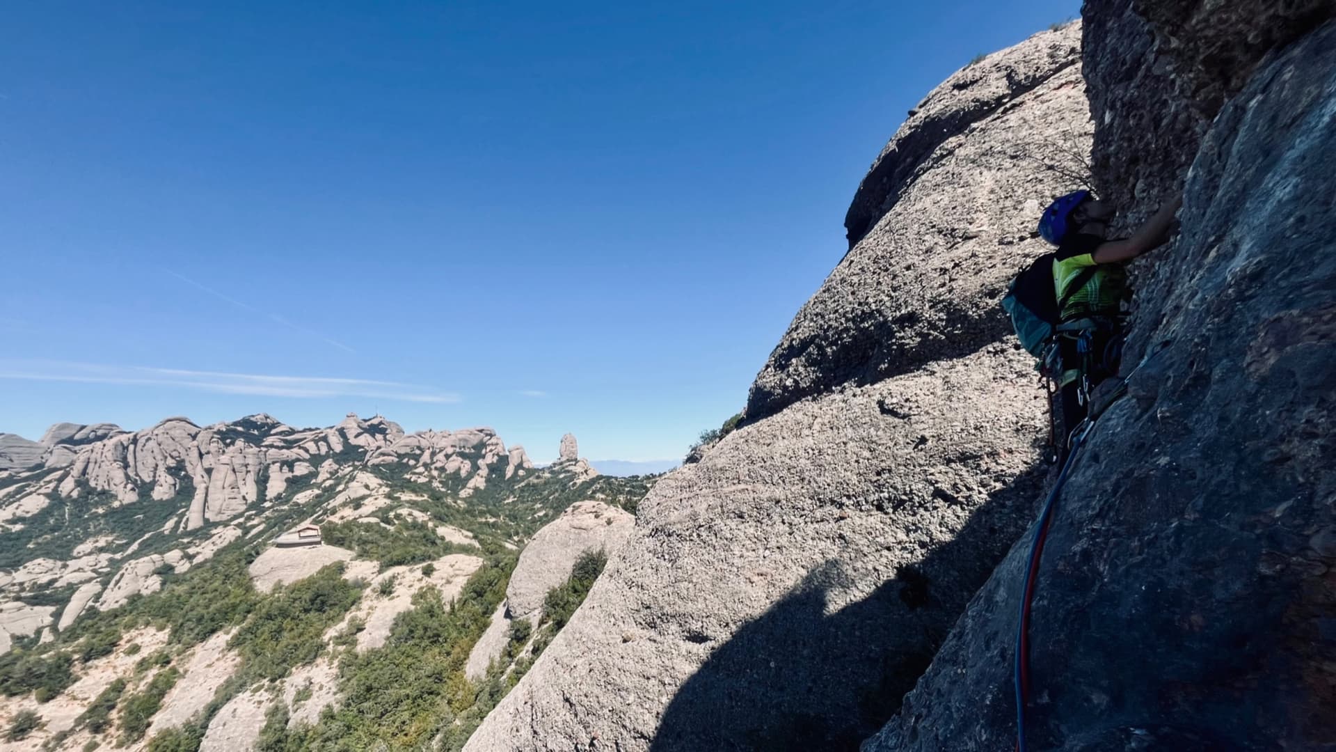 A climber on La Infidel on the Cara de Mico in April 2026, with the Montserrat needles behind.