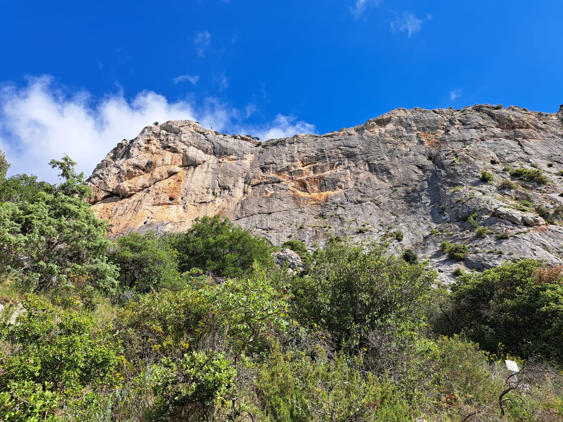The south face of the Chaîne du Clapis above the Vistemboir sector, photographed from the approach by a party on the Diagonale des Vires Rouges, which slants left across the orange-streaked upper wall. The line is not marked.