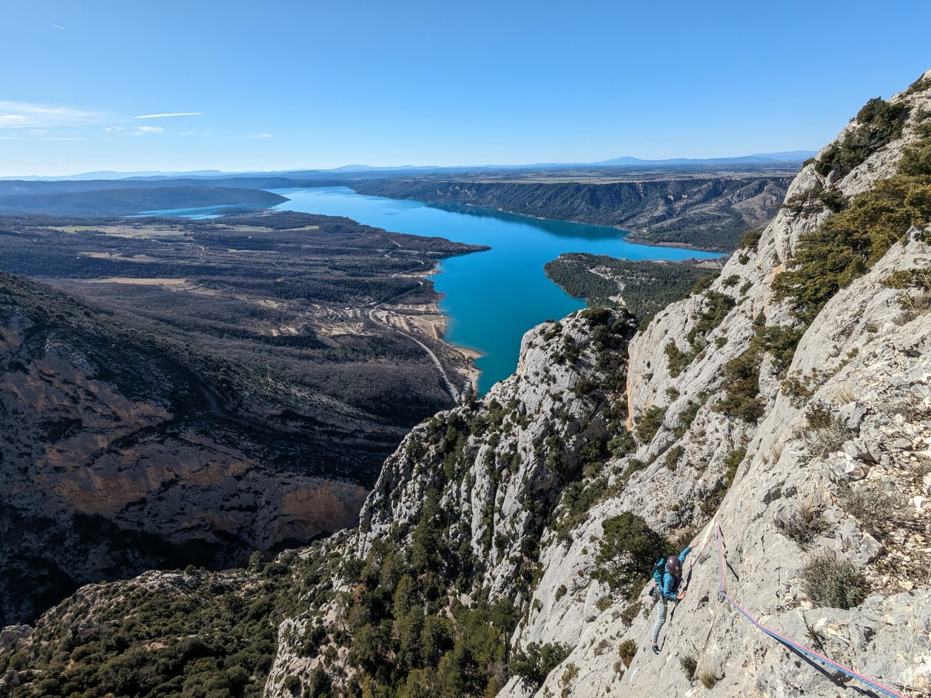 Pitch 5 of Dans les Yeux d'Hervé: a climber low on the grey limestone of Galetas supérieur, with the Lac de Sainte-Croix beyond.