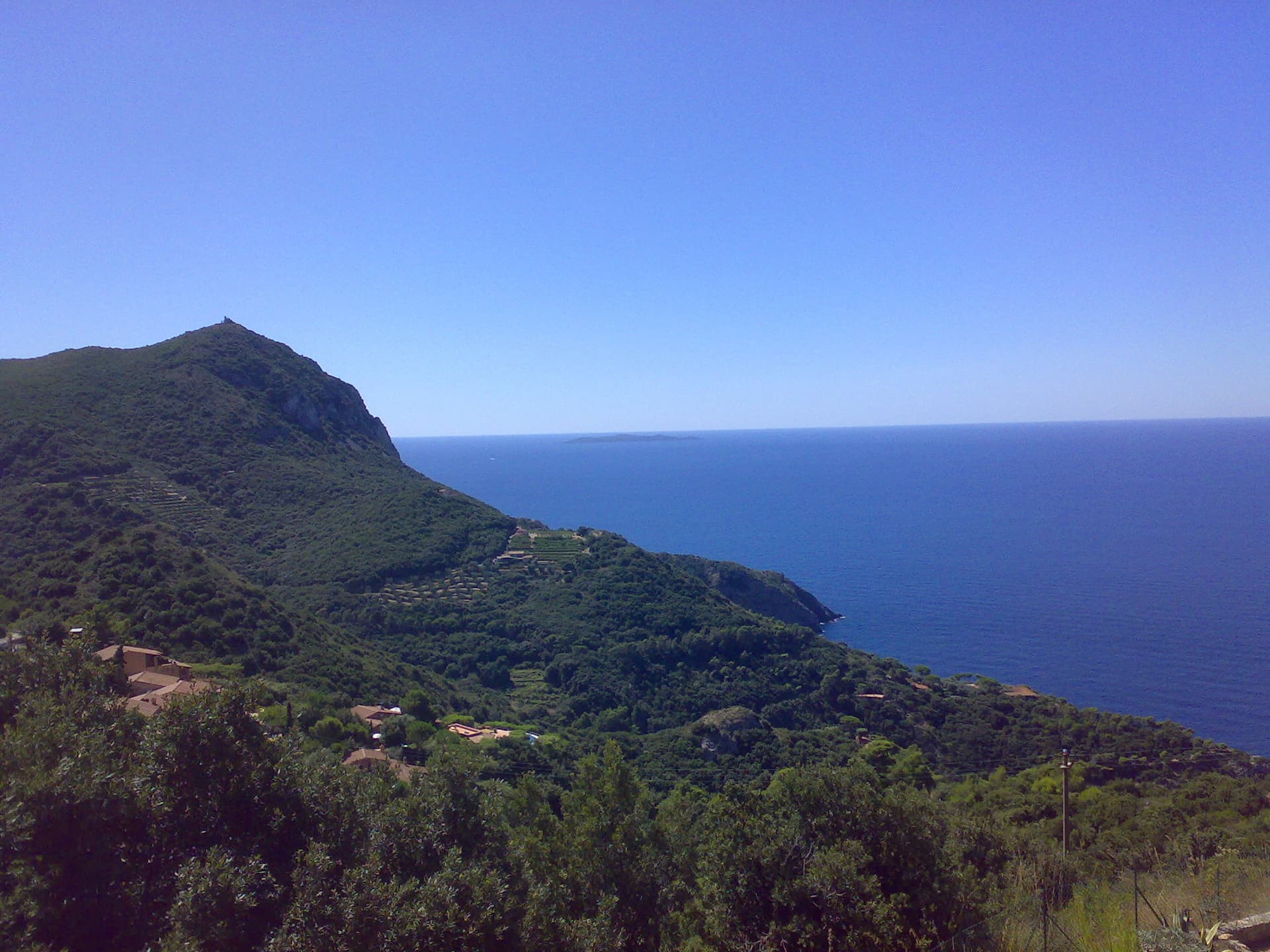 The headland of Capo d'Uomo on Monte Argentario with its watchtower on top, and the island of Giannutri on the horizon. The multipitch wall drops towards the sea below the tower; the routes are not visible in this view.