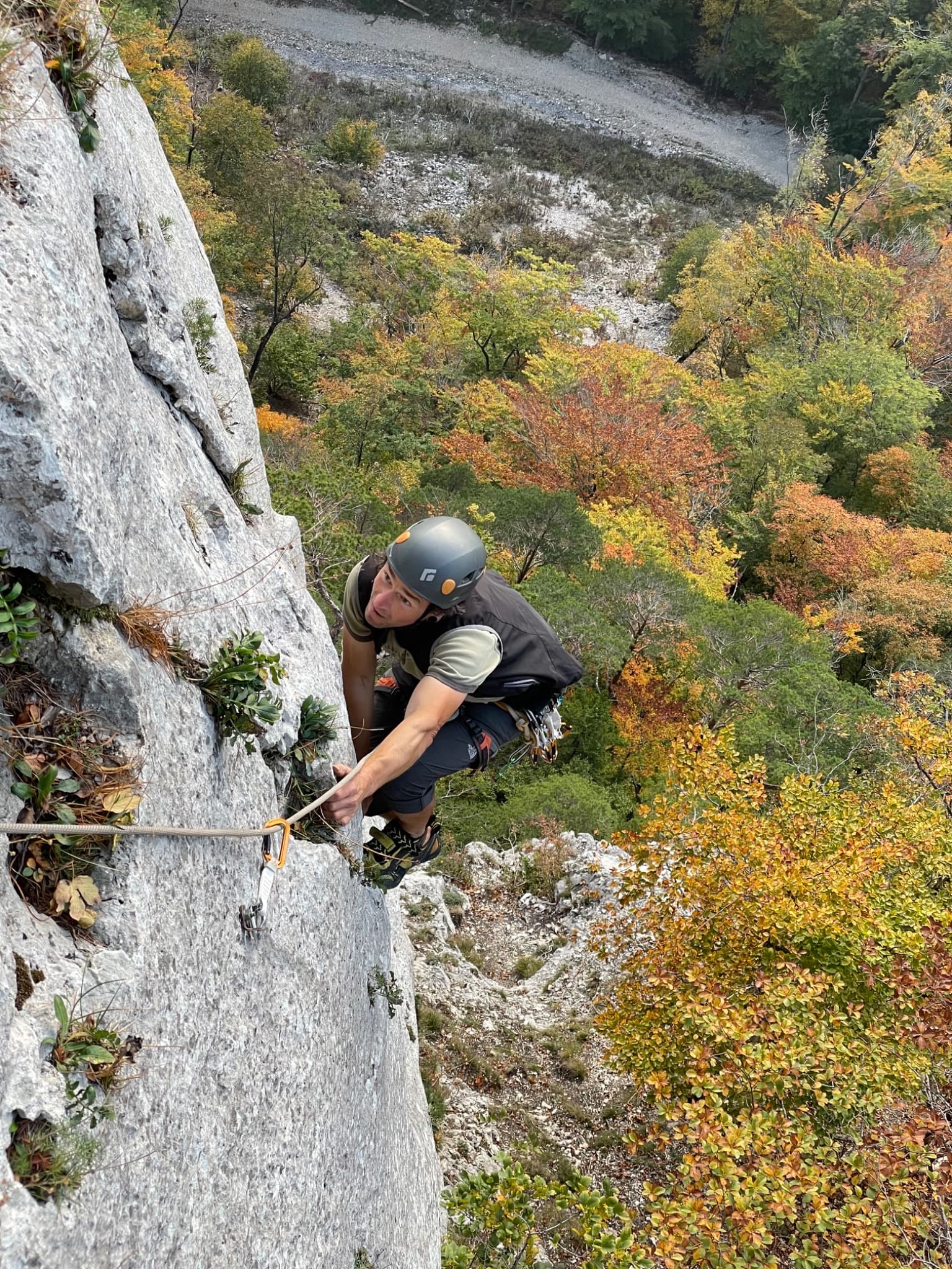 A climber on pitch 3 of The Wall, Plagne, above the autumn woods