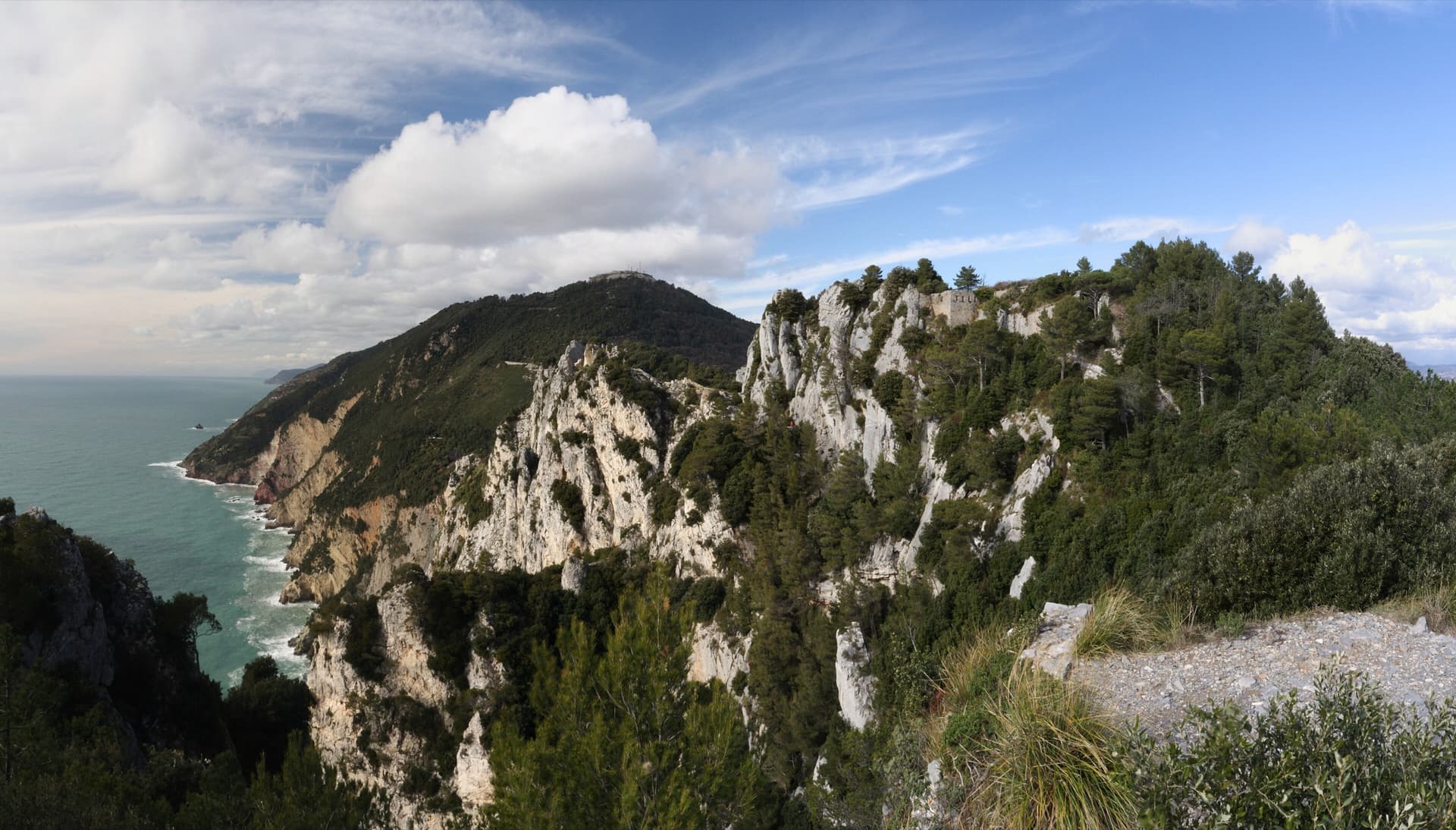 The white limestone cliffs of Monte Muzzerone falling towards the Ligurian Sea, with the walls of the old fort on the crest.