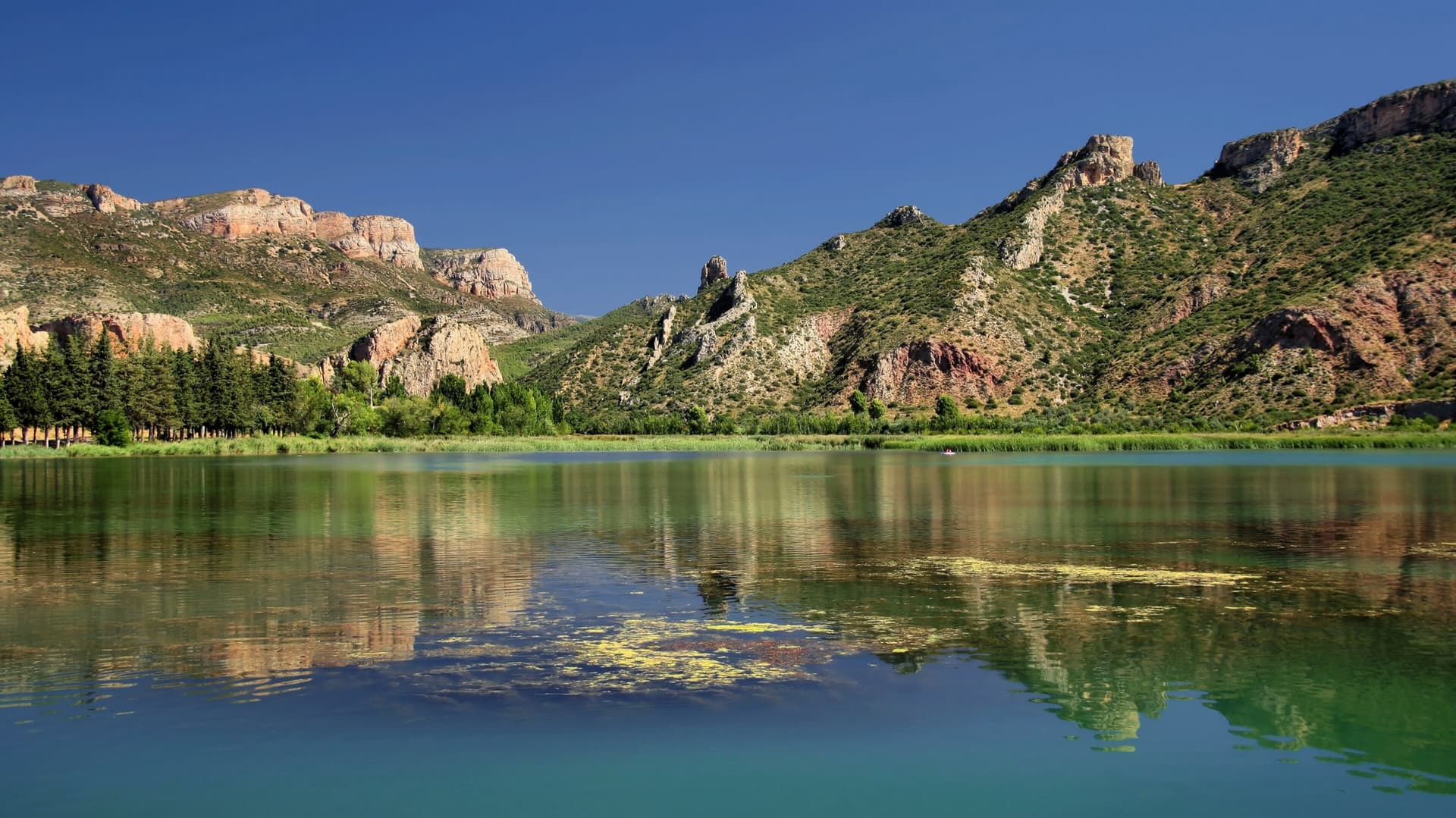 The crags above the Sant Llorenç de Montgai reservoir on the Segre, reflected in the still water on a clear summer day.