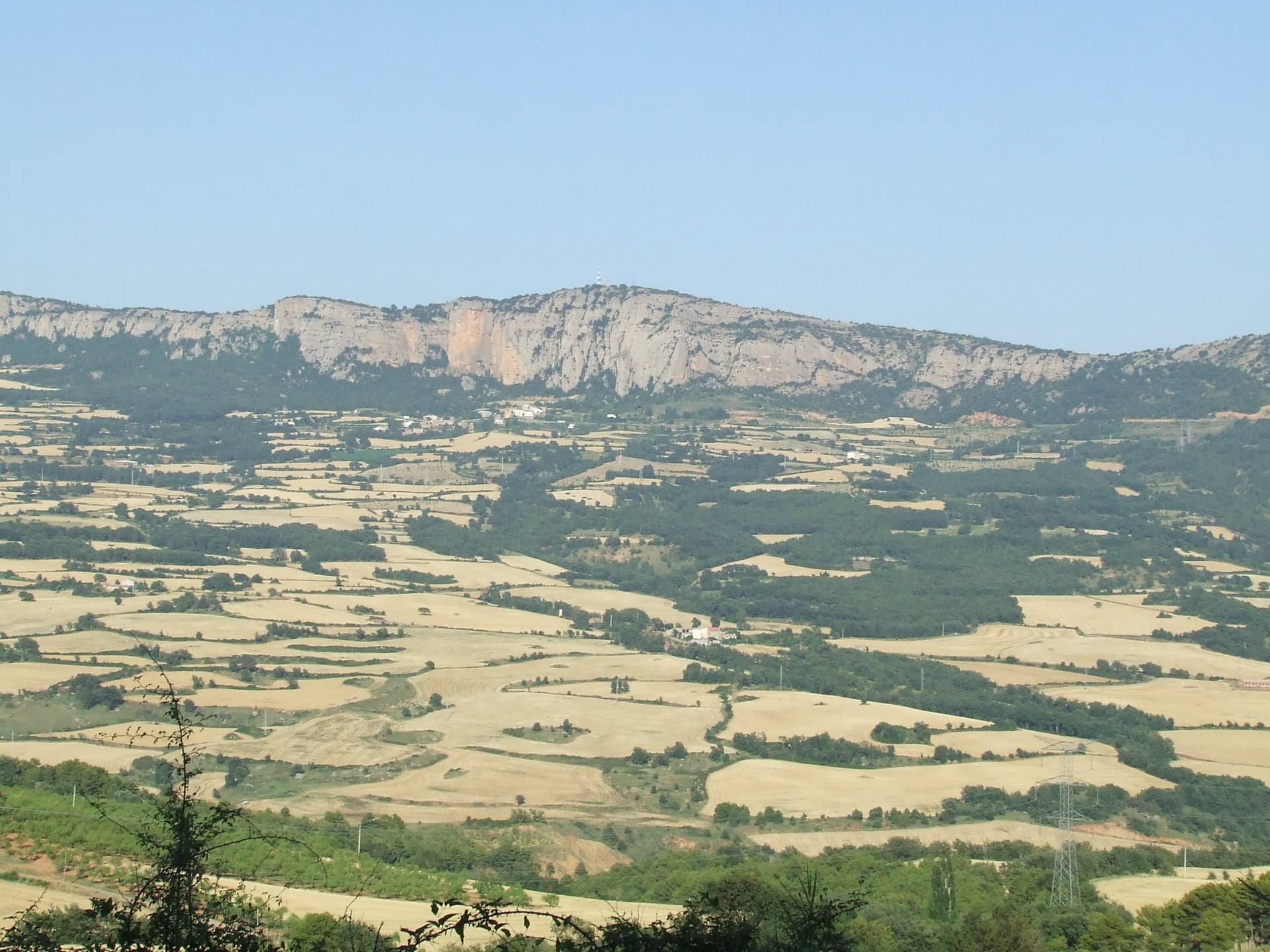 The cliffs of the Roc de Benavent above the harvested summer fields of the Conca, with the orange walls in the centre of the band.